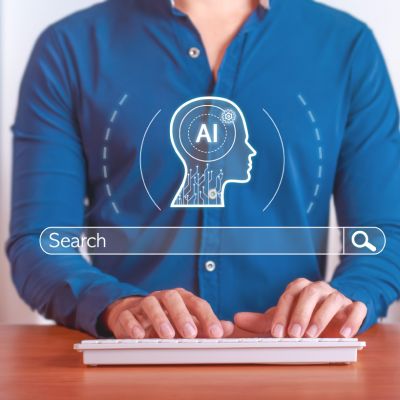 Person typing on a keyboard at a desk with a digital AI head icon and search bar overlay
